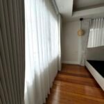 A room interior with gray and white curtains, wood floors, and a bed.