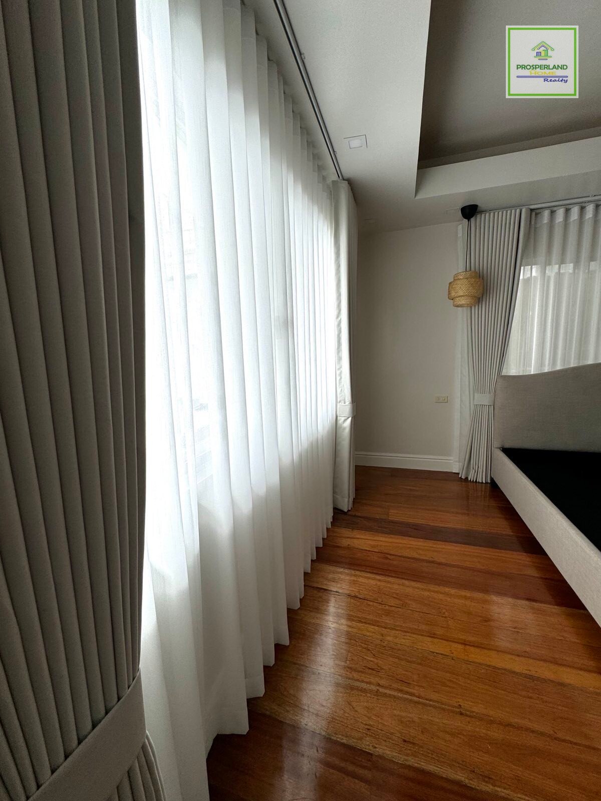 A room interior with gray and white curtains, wood floors, and a bed.