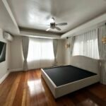 Bright bedroom with wood floors, a black mattress on a beige platform bed, sheer curtains, and a ceiling fan.