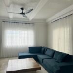 A modern living room with a blue sectional sofa, wood coffee table, and white sheer curtains.