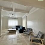 A bright living room with a dark blue sectional, two gray armchairs, and beige tile flooring.