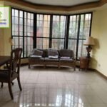 A living room area with a dining table, sofa, and large windows.