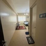 Hallway leading to a small apartment room with a bed, table, and rug.