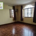 An empty room with hardwood floors, windows with curtains, and tan walls.