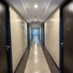 A straight, well-lit hotel or apartment hallway with numbered doors.