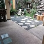 Outdoor patio area with stepping stones, gravel, and a grotto with a statue.