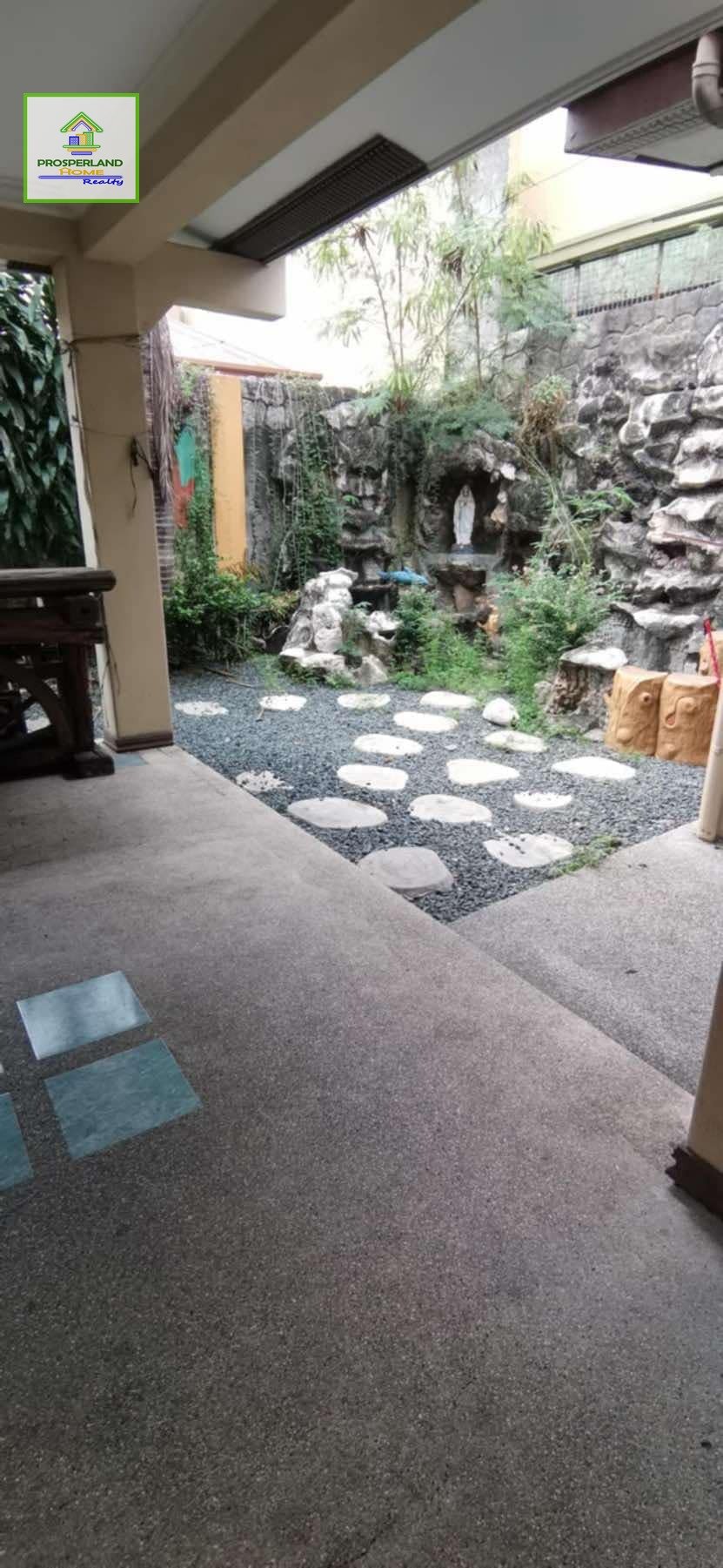 Outdoor patio area with stepping stones, gravel, and a grotto with a statue.