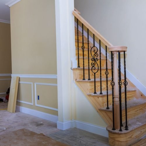 Staircase with wood treads and black wrought iron spindles in a new home under construction.