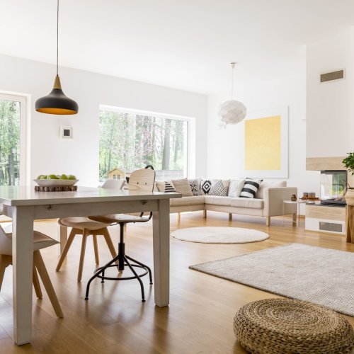 Bright, modern living room with a dining table, sofa, hardwood floors, and black pendant lamp.