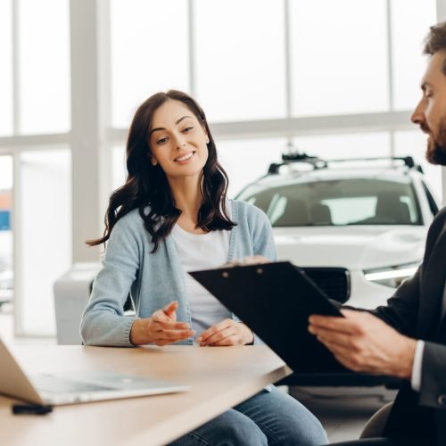 A car salesman showing a contract to a smiling customer in a dealership.