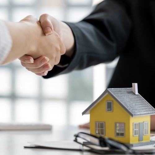 Handshake over a house model, symbolizing a real estate deal.