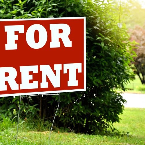 A red and white "FOR RENT" sign in a grassy yard.