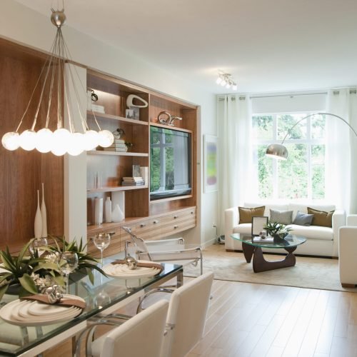 Modern living room and dining room with a glass table, white chairs, and a built-in media center.