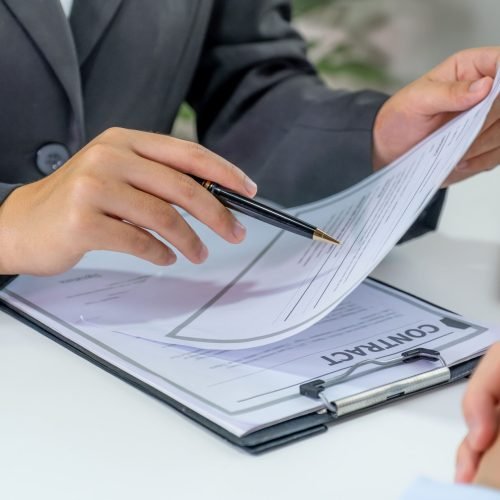 Person reviews a contract on a clipboard, holding a pen.