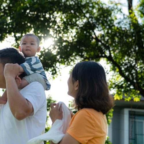A family enjoys time together outdoors, with a baby riding on dad's shoulders.