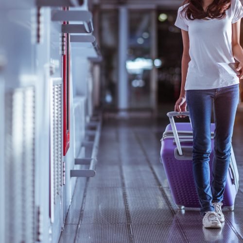A young woman pulls a purple suitcase in a modern airport.